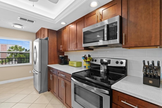 kitchen featuring light tile patterned floors, backsplash, stainless steel appliances, and a tray ceiling