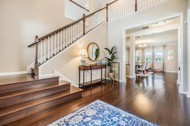 foyer entrance featuring ornamental molding, a towering ceiling, an inviting chandelier, and dark hardwood / wood-style flooring