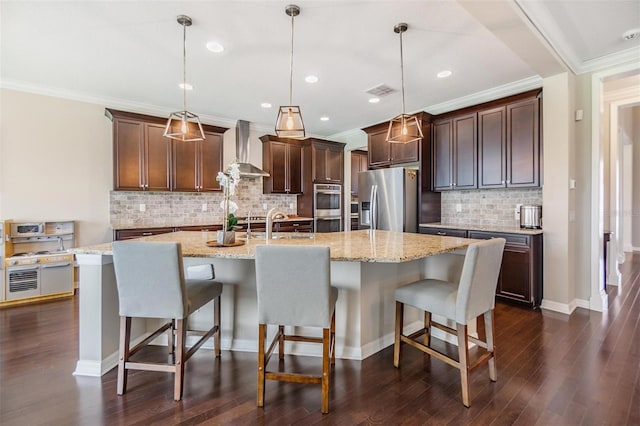 kitchen with stainless steel appliances, a large island, hanging light fixtures, and wall chimney range hood