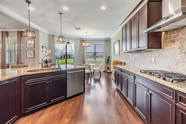 kitchen featuring sink, decorative light fixtures, dark brown cabinets, stainless steel appliances, and wall chimney range hood