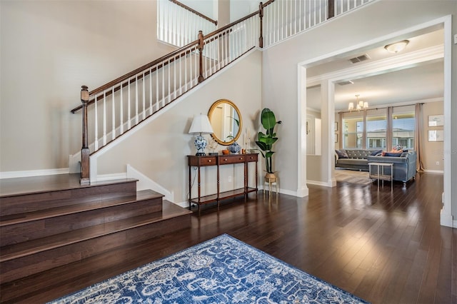 staircase featuring baseboards, visible vents, an inviting chandelier, hardwood / wood-style flooring, and a towering ceiling