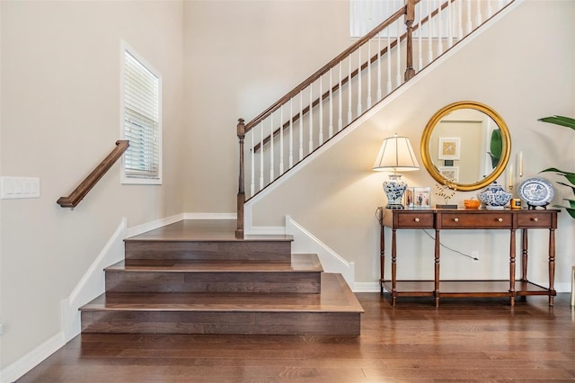 stairway with a high ceiling, baseboards, and wood finished floors