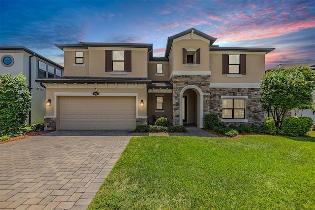 view of front facade featuring an attached garage, stucco siding, a front lawn, stone siding, and decorative driveway