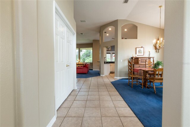 corridor with lofted ceiling, a notable chandelier, and light colored carpet