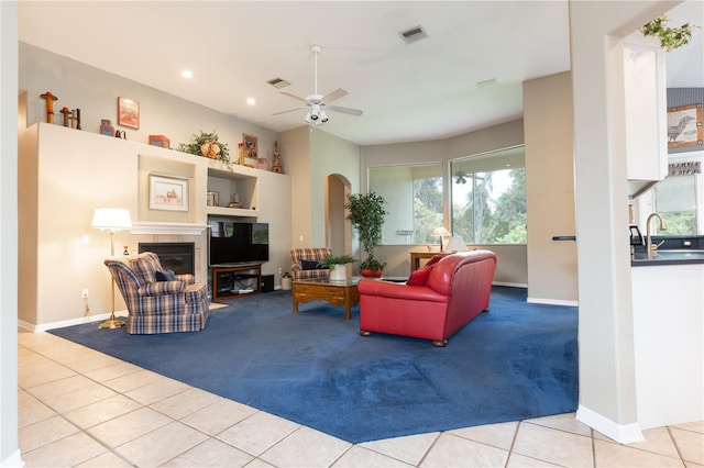 tiled living room featuring a tile fireplace, sink, and ceiling fan