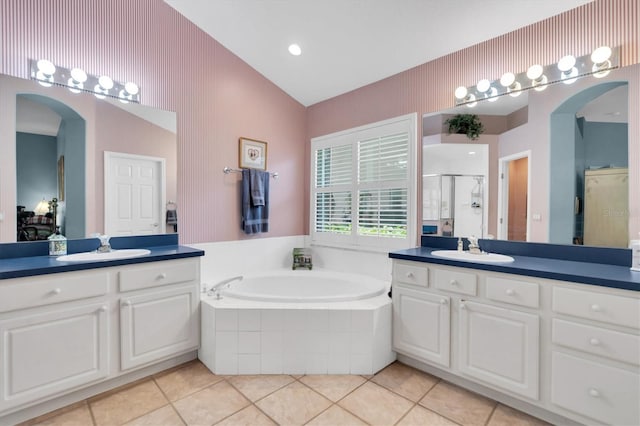 bathroom with a relaxing tiled tub, double vanity, tile patterned flooring, and vaulted ceiling