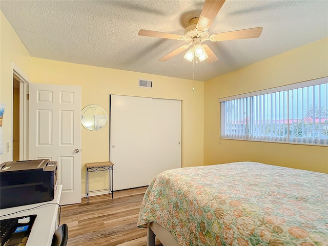 bedroom with light hardwood / wood-style floors, a textured ceiling, a closet, and ceiling fan