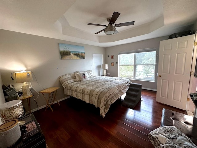 bedroom with ceiling fan, wood-type flooring, and a tray ceiling