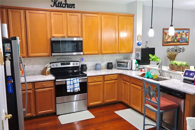 kitchen with sink, appliances with stainless steel finishes, dark hardwood / wood-style floors, light stone countertops, and decorative light fixtures