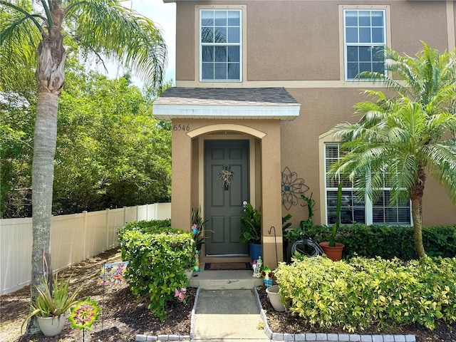 6546 Marlberry Way, Largo, FL 33773 - doorway to property with roof with shingles, stucco siding, and fence