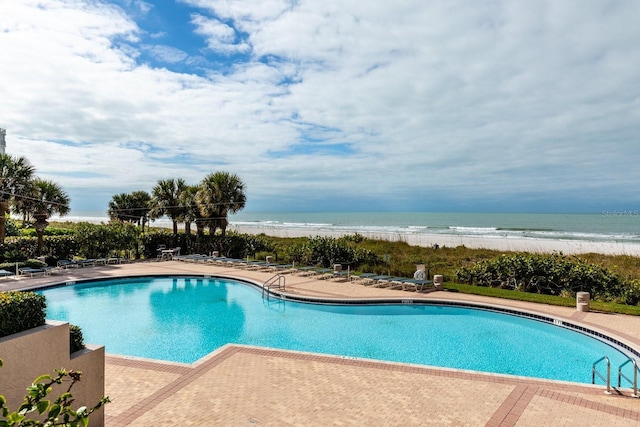 community pool with a view of the beach, a patio area, and a water view