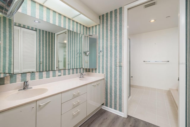 full bathroom featuring a stall shower, wood finished floors, a sink, and wallpapered walls