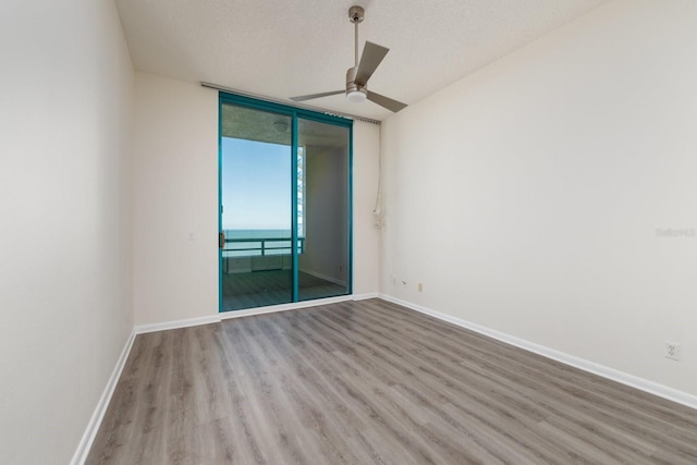 unfurnished room with a textured ceiling, baseboards, a wall of windows, and wood finished floors