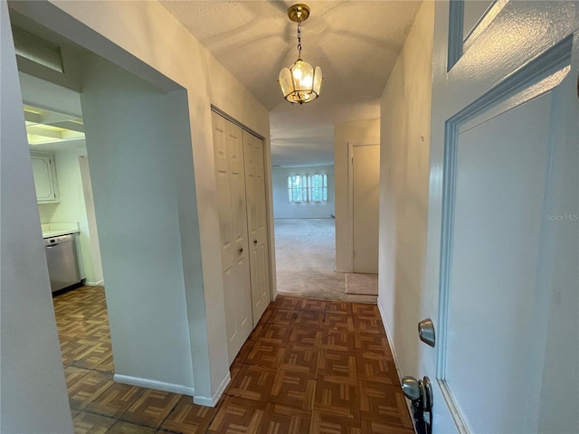 hall with dark colored carpet, an inviting chandelier, and a textured ceiling