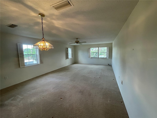 spare room with carpet flooring, a textured ceiling, ceiling fan with notable chandelier, and plenty of natural light