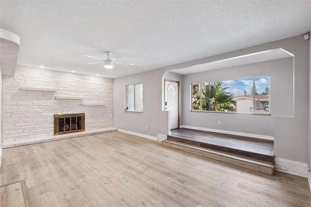 unfurnished living room featuring ceiling fan, a fireplace, light hardwood / wood-style floors, and a textured ceiling