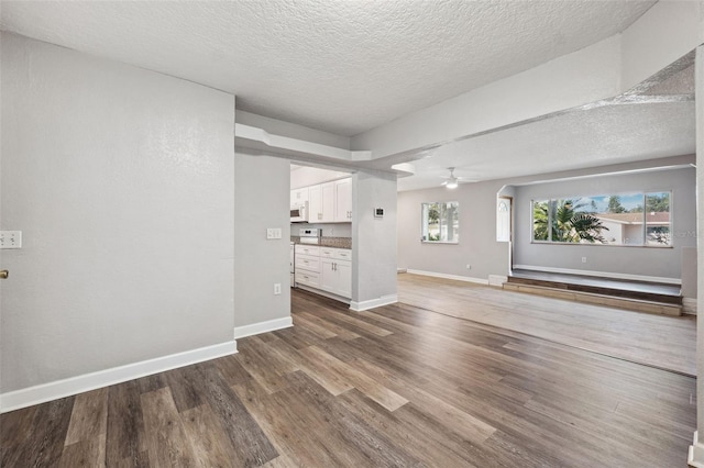 unfurnished living room featuring ceiling fan, a textured ceiling, and dark hardwood / wood-style flooring