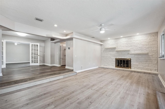 unfurnished living room featuring hardwood / wood-style flooring, ceiling fan, a textured ceiling, and a fireplace