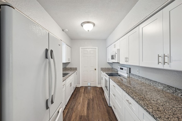 kitchen featuring dark wood-type flooring, dark stone countertops, white cabinets, and white appliances