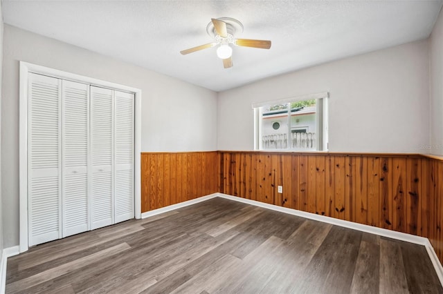 unfurnished bedroom with hardwood / wood-style flooring, wooden walls, a closet, and a textured ceiling