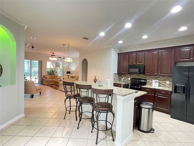 kitchen featuring light tile patterned floors, a breakfast bar, tasteful backsplash, black appliances, and an island with sink