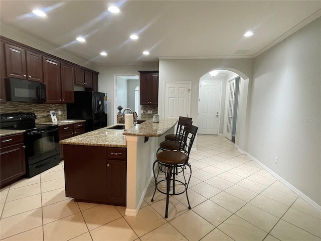 kitchen featuring an island with sink, sink, a kitchen breakfast bar, black appliances, and crown molding