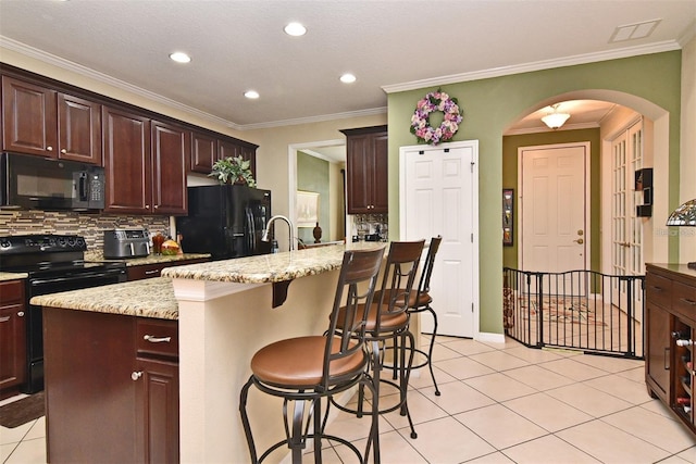 kitchen featuring a center island with sink, light stone countertops, black appliances, a kitchen bar, and light tile patterned flooring