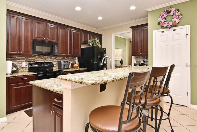 kitchen featuring an island with sink, light tile patterned floors, a kitchen breakfast bar, and black appliances