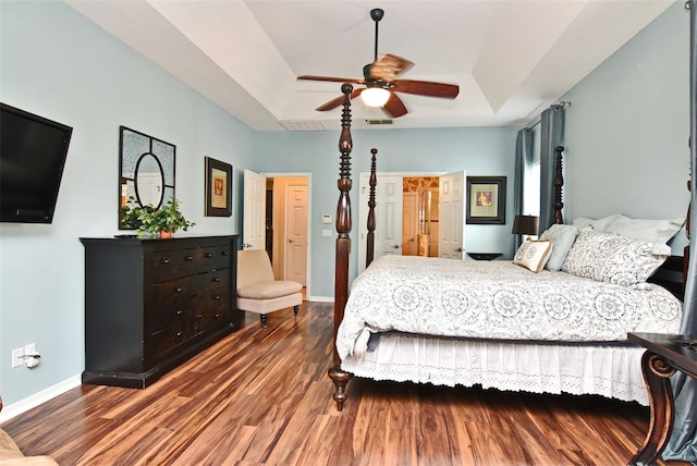 bedroom with dark hardwood / wood-style floors, ceiling fan, and a tray ceiling