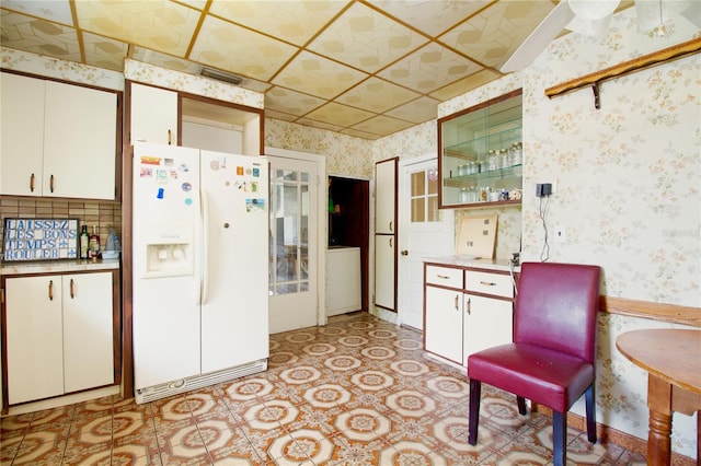 kitchen featuring white fridge with ice dispenser, white cabinets, and wallpapered walls