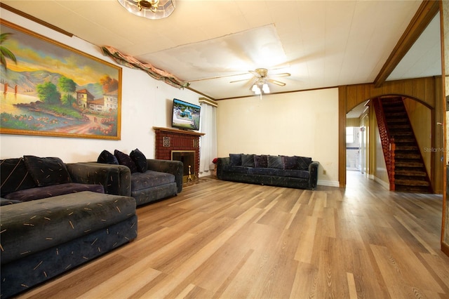 living room with arched walkways, a fireplace, stairway, a ceiling fan, and wood finished floors