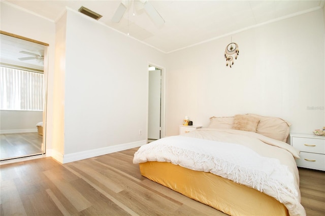 bedroom with wood finished floors, a ceiling fan, visible vents, baseboards, and ornamental molding