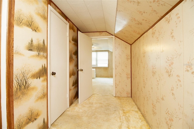 hallway featuring vaulted ceiling, wallpapered walls, and light colored carpet