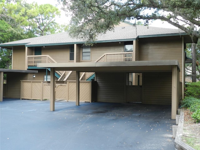 rear view of property featuring stairs, a carport, aphalt driveway, and a shingled roof