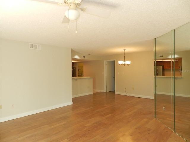 interior space featuring baseboards, visible vents, wood finished floors, a textured ceiling, and ceiling fan with notable chandelier