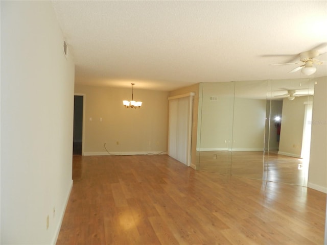 unfurnished room with ceiling fan with notable chandelier, light wood finished floors, visible vents, and baseboards