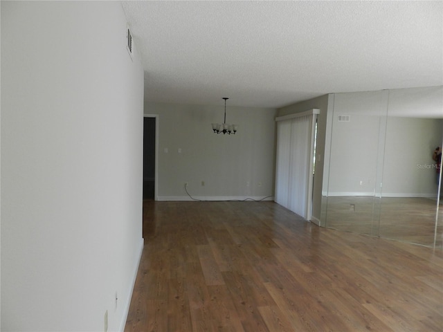 unfurnished room featuring visible vents, a textured ceiling, an inviting chandelier, and wood finished floors