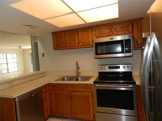 kitchen featuring brown cabinetry, appliances with stainless steel finishes, a peninsula, light countertops, and a sink