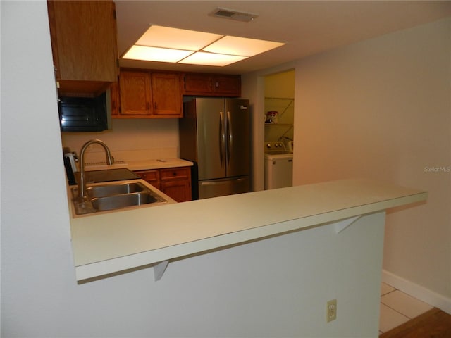 kitchen featuring visible vents, freestanding refrigerator, a peninsula, light countertops, and a sink