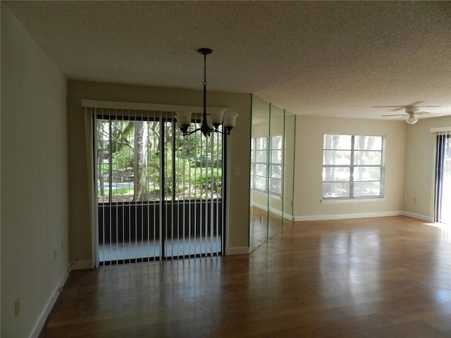 unfurnished dining area featuring a healthy amount of sunlight, a textured ceiling, wood finished floors, and ceiling fan with notable chandelier