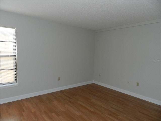 unfurnished room with a textured ceiling, baseboards, and wood finished floors