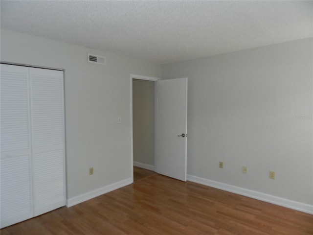 unfurnished bedroom with a textured ceiling, wood finished floors, visible vents, baseboards, and a closet