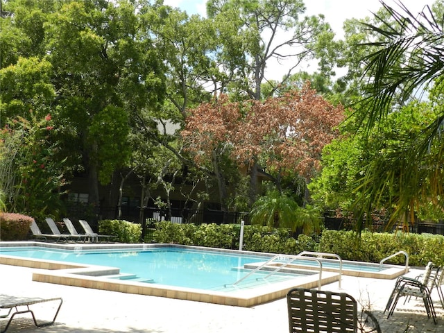 community pool with a patio area, fence, and a jacuzzi