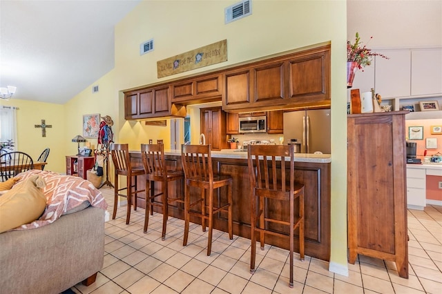 kitchen featuring light tile patterned floors, stainless steel appliances, high vaulted ceiling, a kitchen bar, and kitchen peninsula