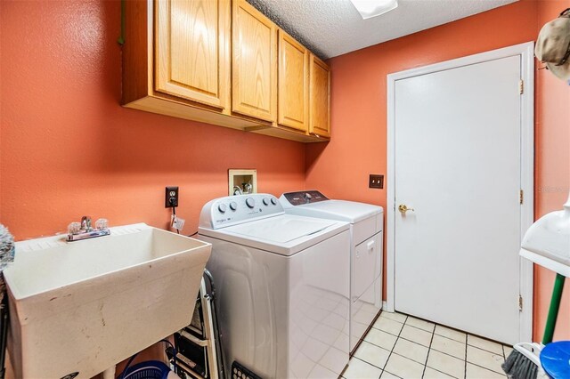 laundry room featuring light tile patterned flooring, sink, cabinets, washing machine and dryer, and a textured ceiling