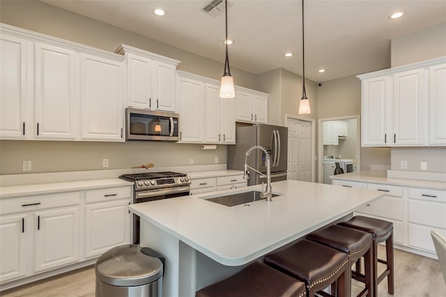 kitchen featuring white cabinetry, sink, a kitchen island with sink, independent washer and dryer, and stainless steel appliances