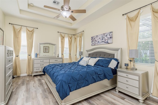 bedroom with a tray ceiling, ceiling fan, and light wood-type flooring