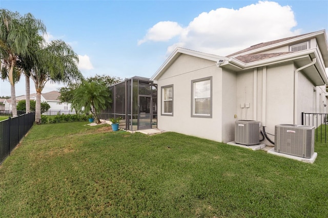 rear view of property featuring central AC, glass enclosure, and a lawn