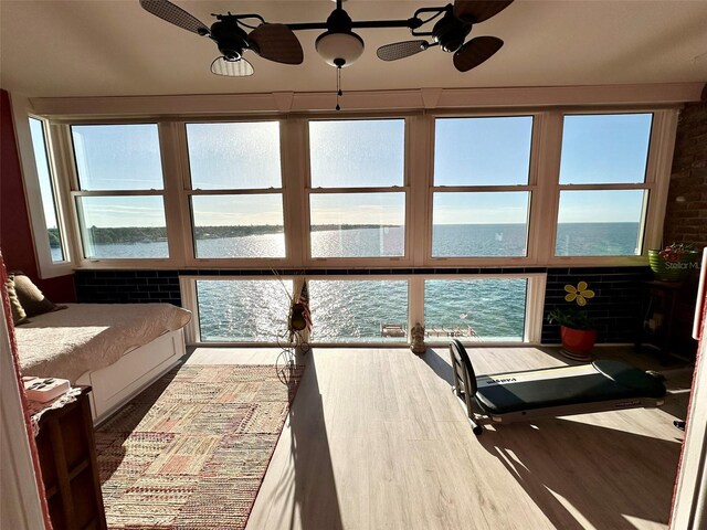 interior space with brick wall, a water view, ceiling fan, and hardwood / wood-style flooring