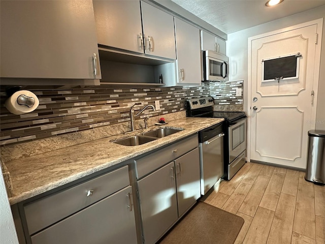 kitchen with sink, gray cabinetry, backsplash, stainless steel appliances, and light hardwood / wood-style flooring